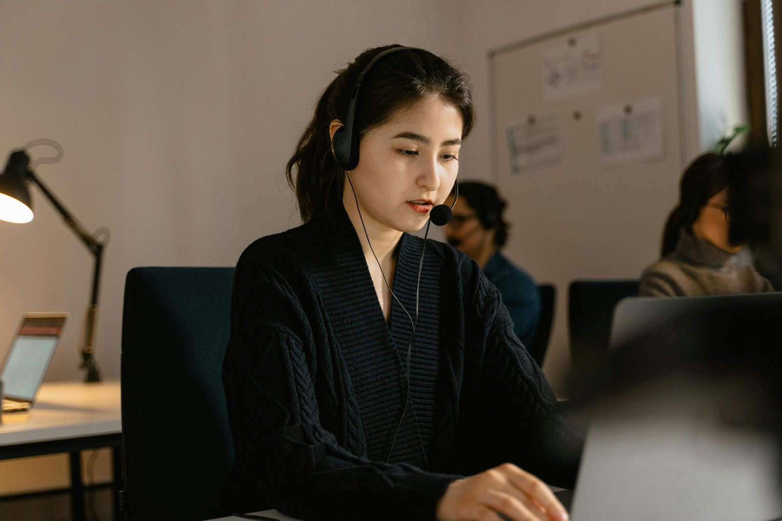 Asian woman in a modern call center, focused on customer support wearing headset.